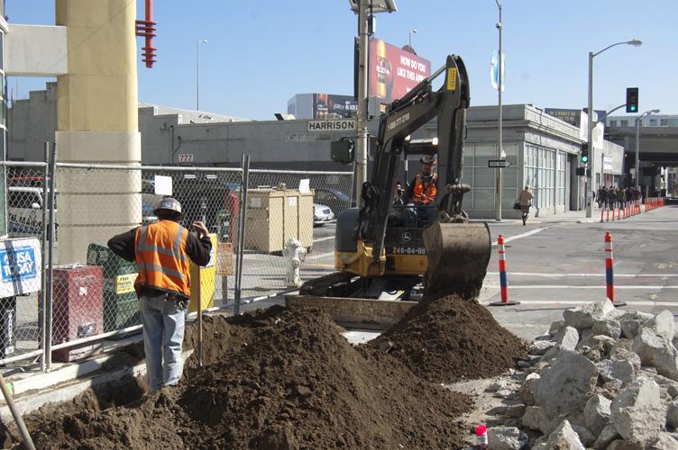 Construction crew operates excavator to dig trench on 4th Street between Folsom and Harrison for ground improvement work.