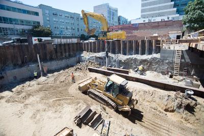 Construction site with excavator, steel sheet piling, and workers in urban trench excavation.