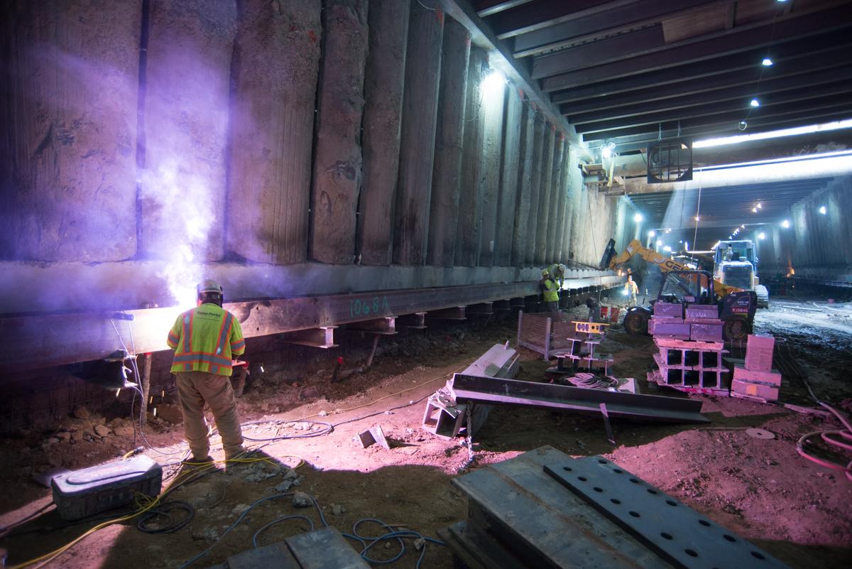 Worker in safety vest welding steel beam in underground station construction area with purple sparks.