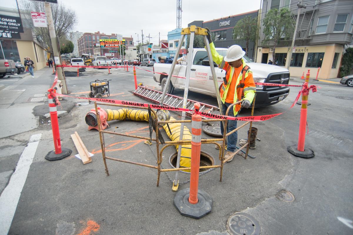 Worker in safety gear installing high-pressure water line in street with equipment and barriers.