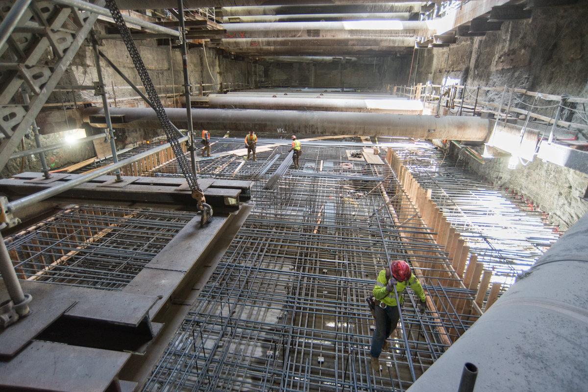 Workers install rebar reinforcement for station headhouse invert slab construction in underground cavern.