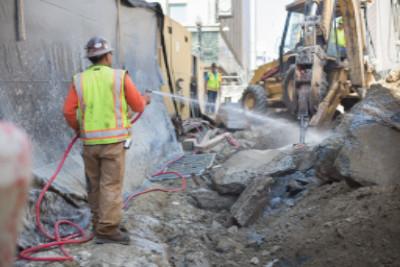 Worker in safety vest operating jackhammer with water spray at Geary and Stockton Street construction site.