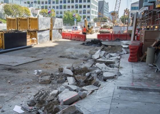 Construction site on 4th Street with excavated pavement and debris, downtown buildings visible in background.