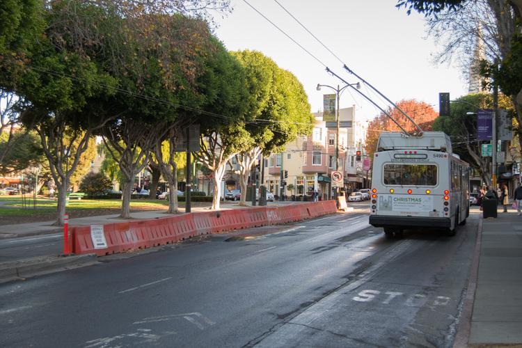 Transit bus on Columbus Avenue with red construction barriers and tree-lined street.