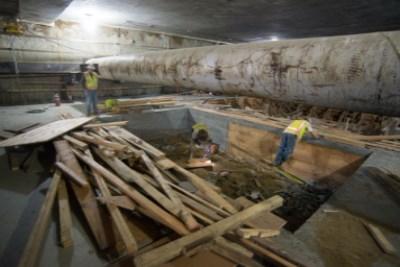 Workers remove wooden forms from concrete structure in underground transit tunnel.