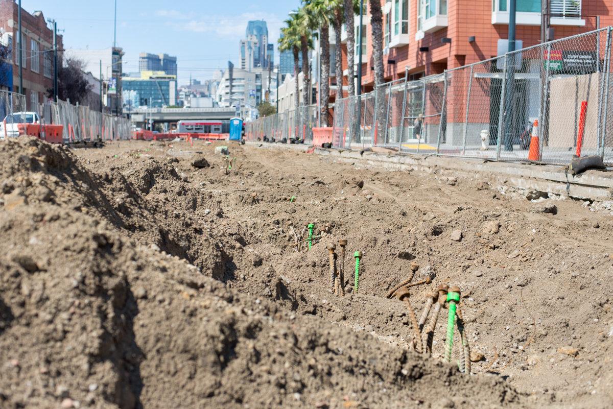 Construction site at 4th and Brannan showing exposed foundation piles with green markers and urban skyline in background.