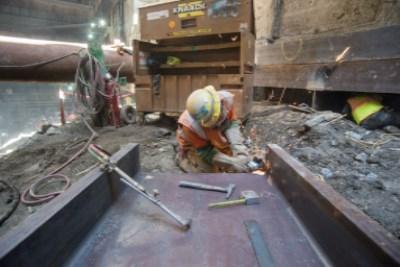 Worker constructing rebar cage in underground transit station headhouse excavation.