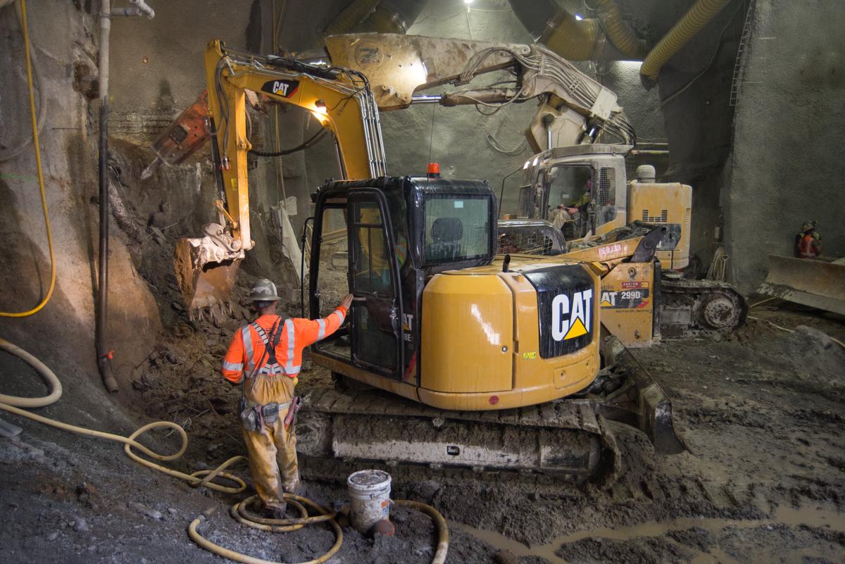 Construction workers operate CAT excavators in underground tunnel cavern during platform excavation work.