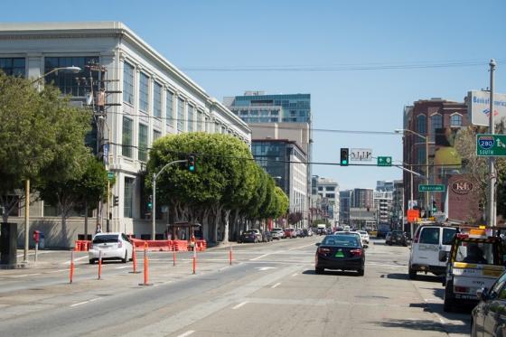 Urban street intersection with traffic barriers, vehicles, and downtown buildings under clear sky.