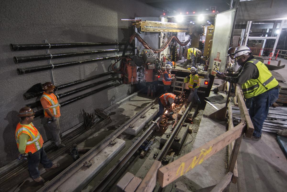 Workers prepare rails for welding on southbound track at transit station platform.
