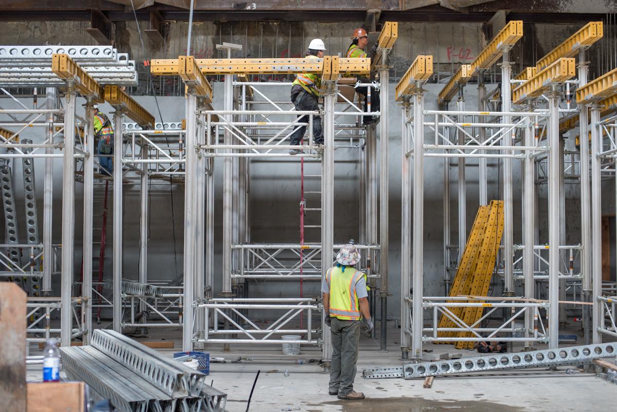 Construction workers assemble concrete forms and steel scaffolding for a transit station headhouse floor slab.