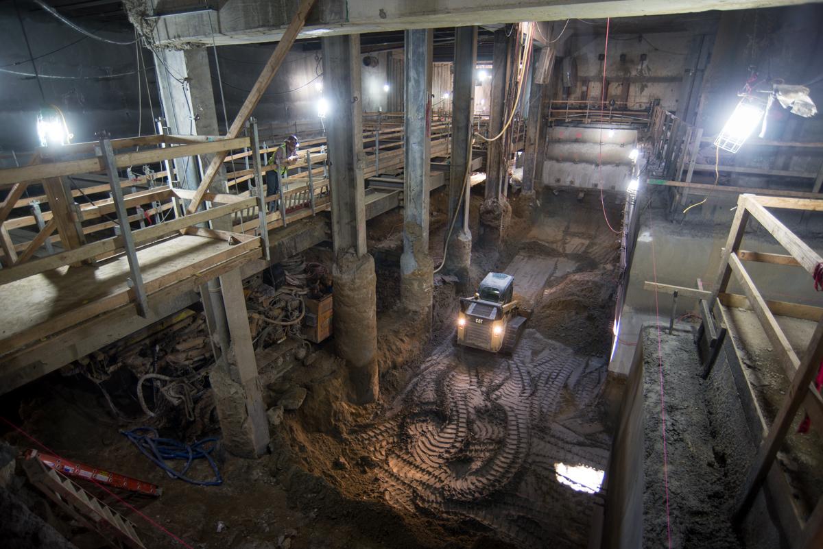 Underground excavation site with wooden support structures, metal columns, and construction equipment inside former garage.