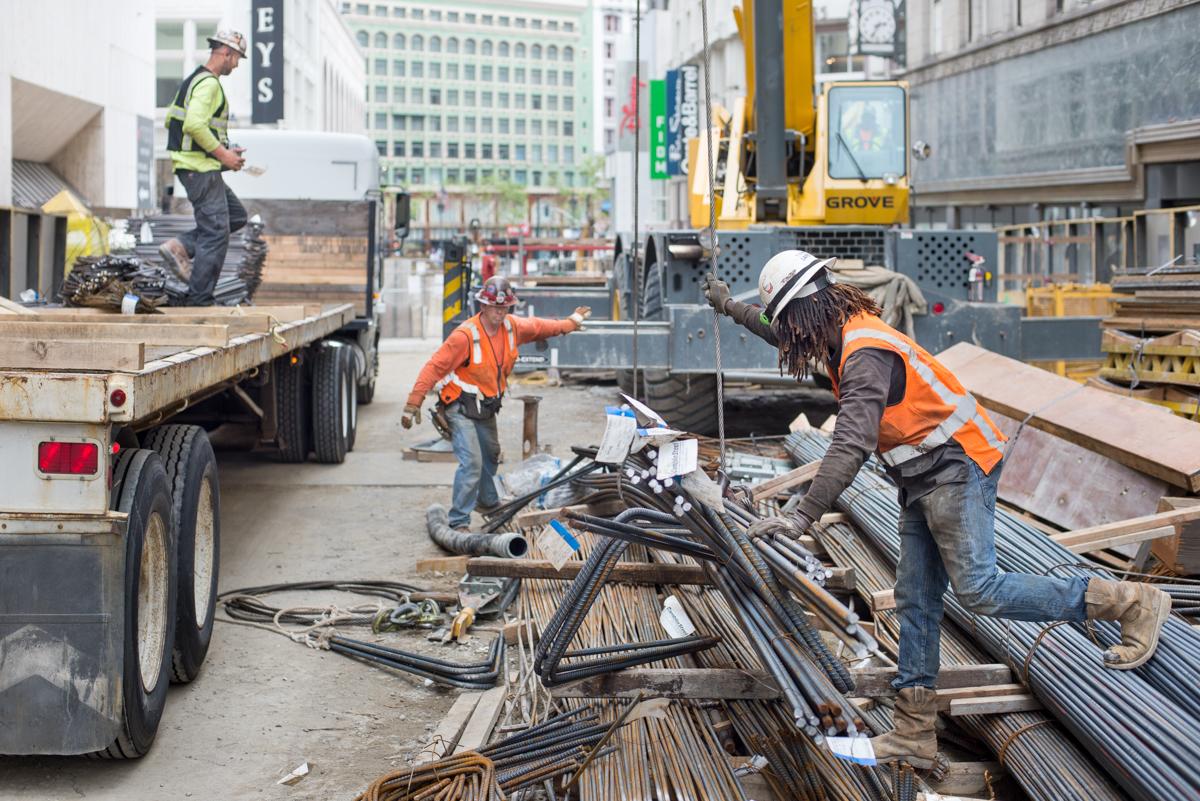Construction workers unload rebar from a flatbed truck at an urban construction site.