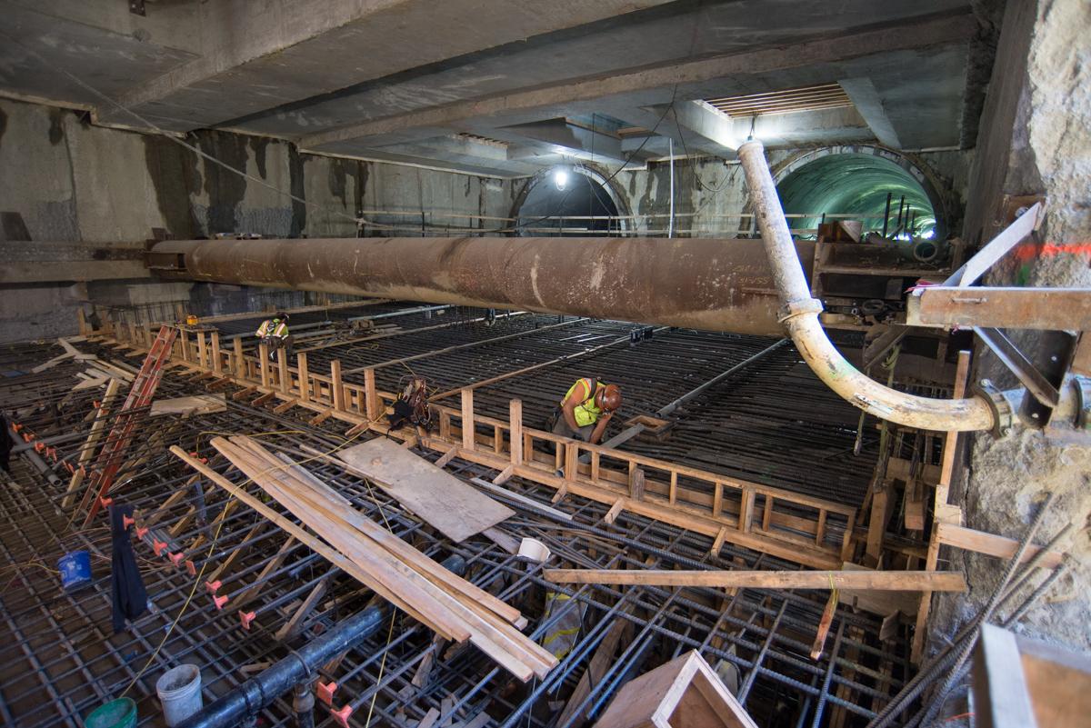 Construction worker on platform level floor slab with rebar cage and wooden formwork at transit station.