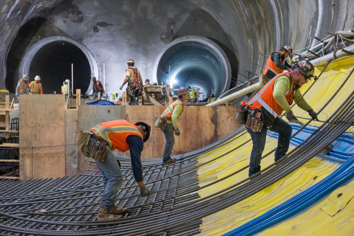 Workers install curved rebar reinforcement in a tunnel under construction for a transit station.