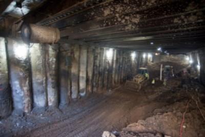 Underground tunnel excavation with wooden support beams and construction equipment visible.