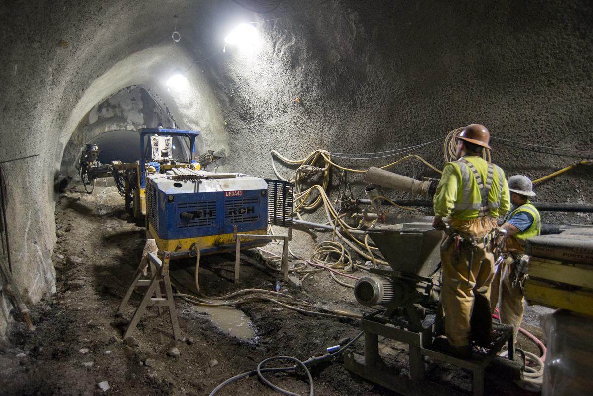 Workers operate a drill rig inside an underground tunnel cavern during transit construction excavation.