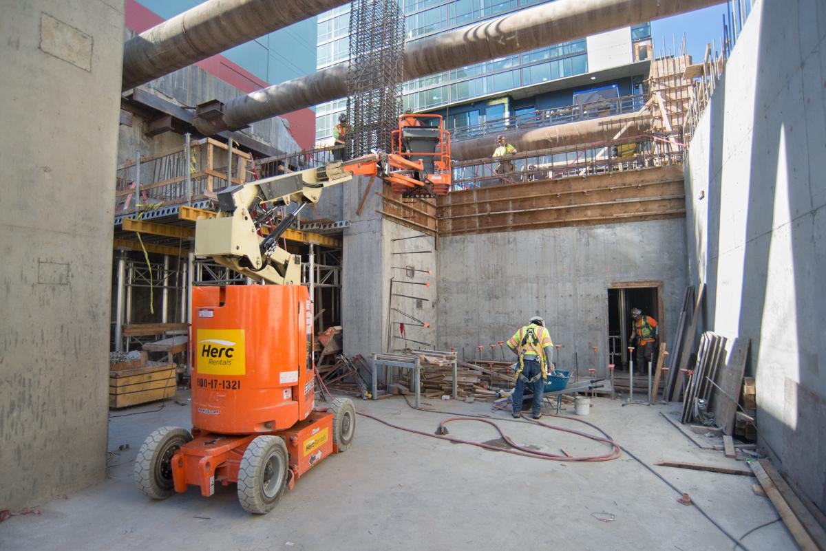 Construction workers and equipment inside concrete headhouse structure during rebar and formwork installation phase.