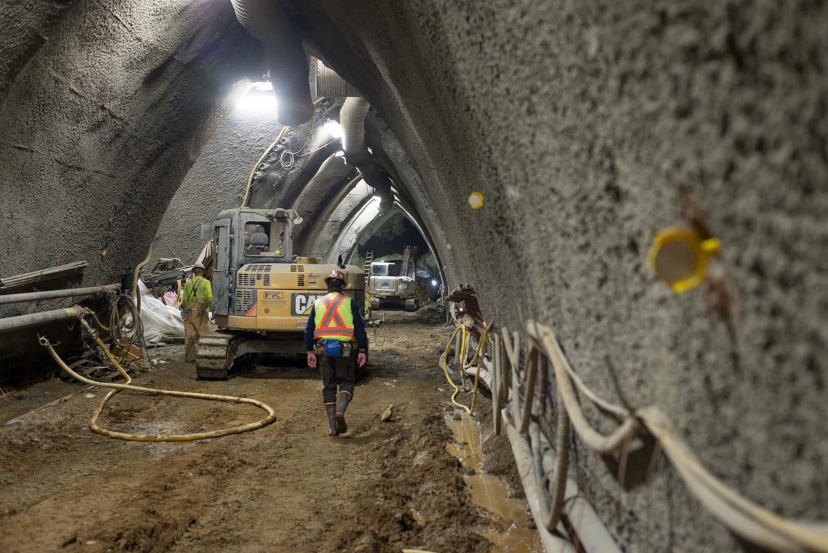 Workers and heavy equipment excavate underground station cavern with concrete walls and survey markings.