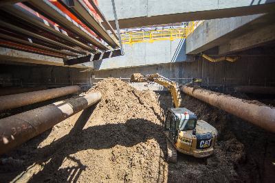 Excavator removing soil from underground transit structure with temporary deck and equipment visible.