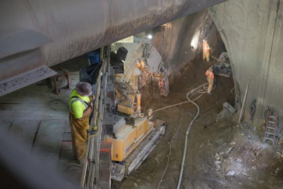 Workers in safety vests spray shotcrete inside underground tunnel excavation for Chinatown Station construction.