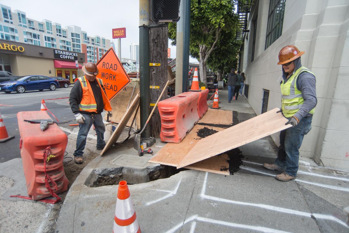 Construction workers cover an open excavation hole with plywood at a street work site.