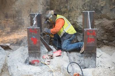 Worker in safety vest grinding metal reinforcing beams during station roof installation on Stockton.