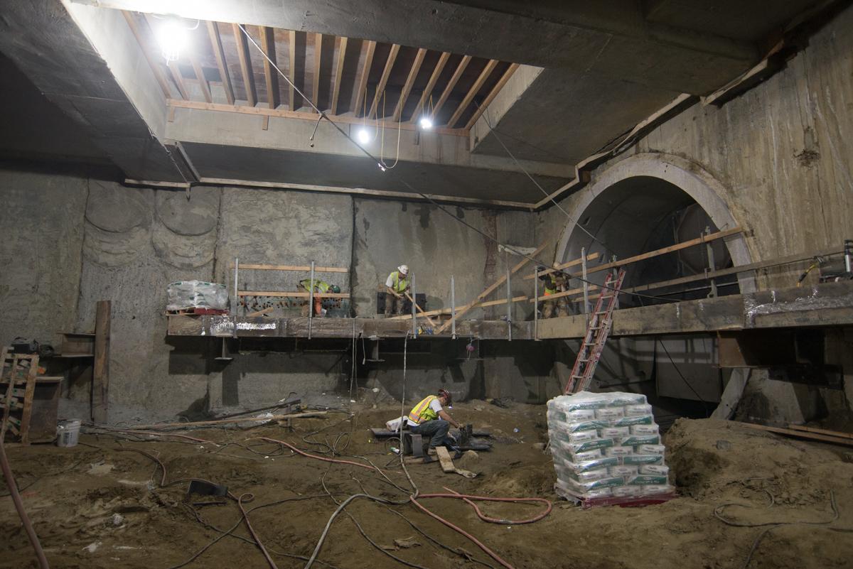 Construction workers perform excavation and ceiling work inside an underground transit station under development.