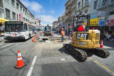 Construction equipment and workers on Stockton Street with traffic cones and a bus nearby.