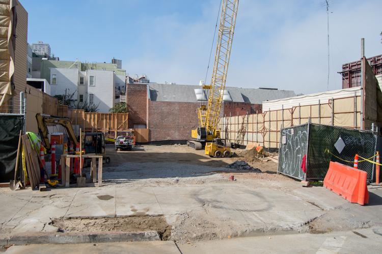 Construction site in North Beach with yellow crane, equipment, and temporary fencing along street.