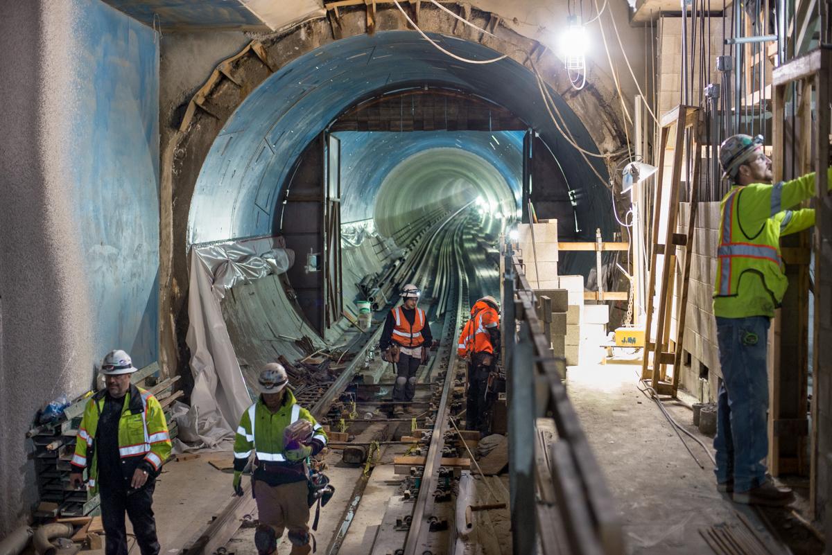 Workers in safety gear install track inside a tunnel section of the Central Subway project.