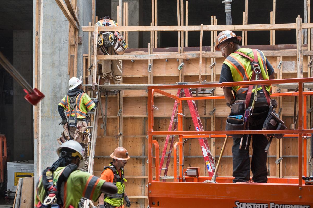 Construction workers on scaffolding and ladder installing concrete forms for escalator supports in transit station headhouse.