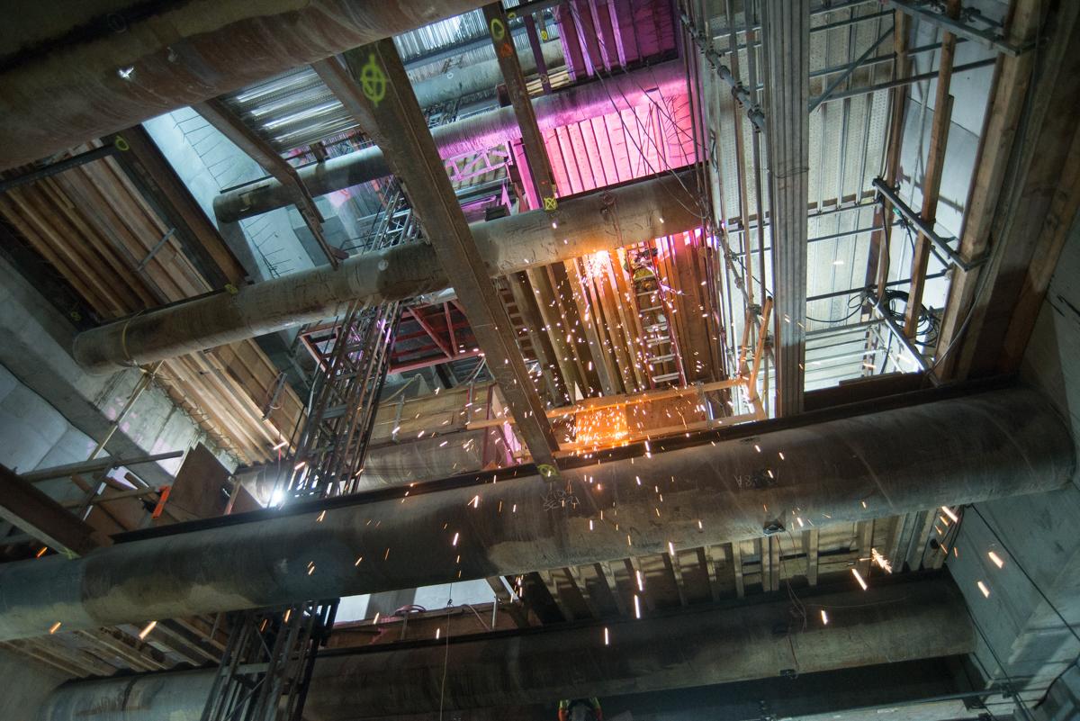 Central Subway construction site showing sparks from welding work on floor decking and temporary shoring removal.
