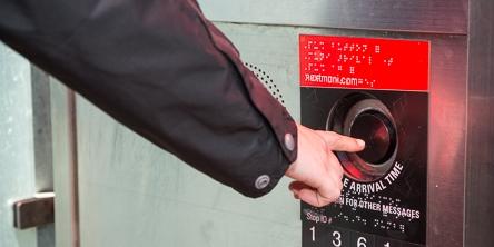 Hand inserting card into NextMuni transit information button on shelter wall.