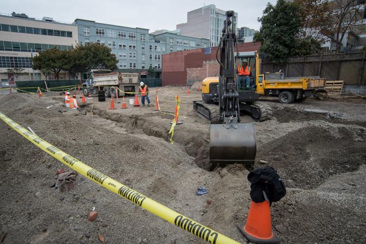 Construction site with excavator, workers in safety vests, yellow caution tape, and dump truck on urban street.