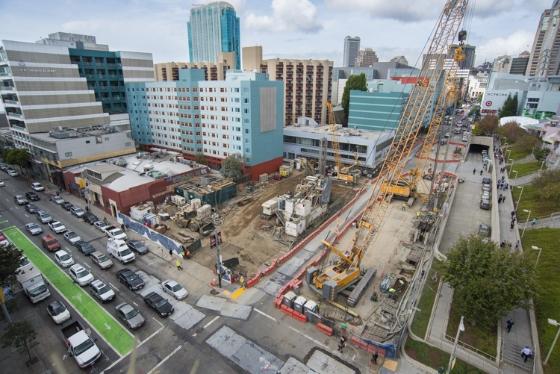 Construction site with cranes and excavation for underground transit station in urban downtown area