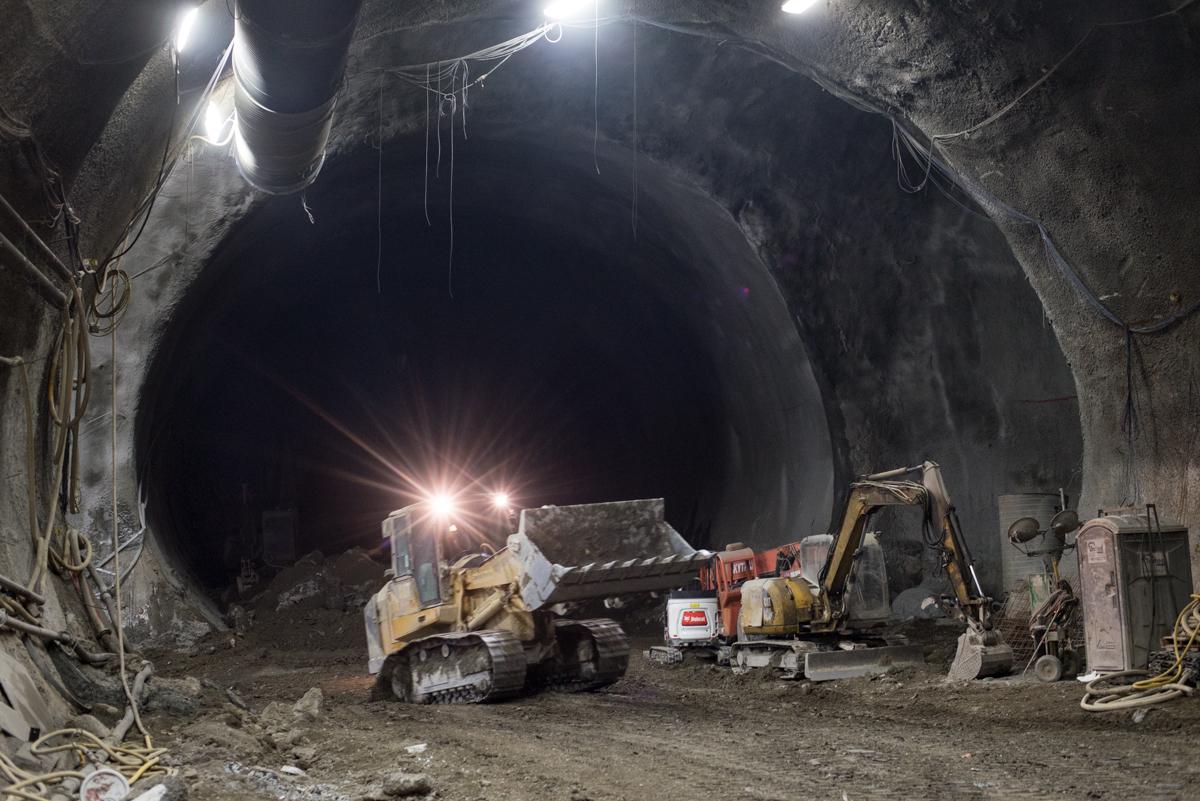 Construction equipment operates inside an illuminated tunnel during underground transit station excavation work.