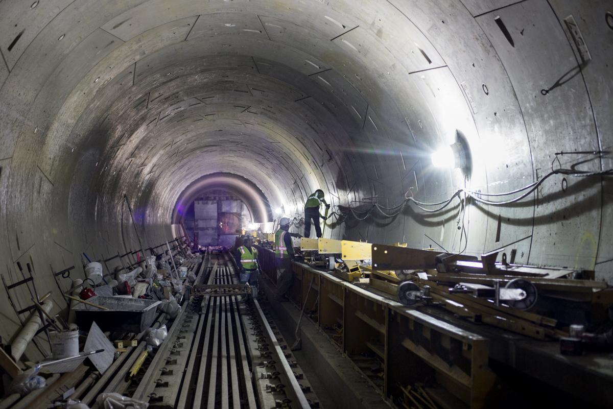 Workers installing track infrastructure inside a concrete transit tunnel during construction.
