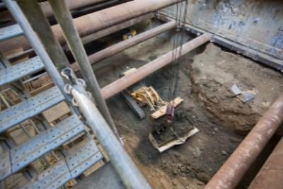 Steel muck bucket filled with excavated soil and debris inside construction headhouse shaft.