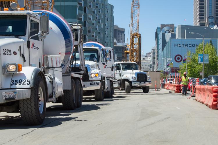 Concrete mixer trucks parked on city street during construction work near downtown buildings and crane.