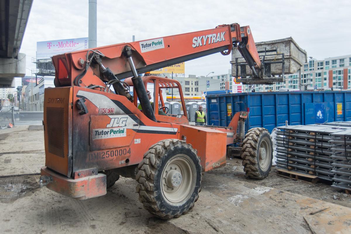 Orange Skytrak telehandler at construction staging area with blue shipping containers and steel materials.