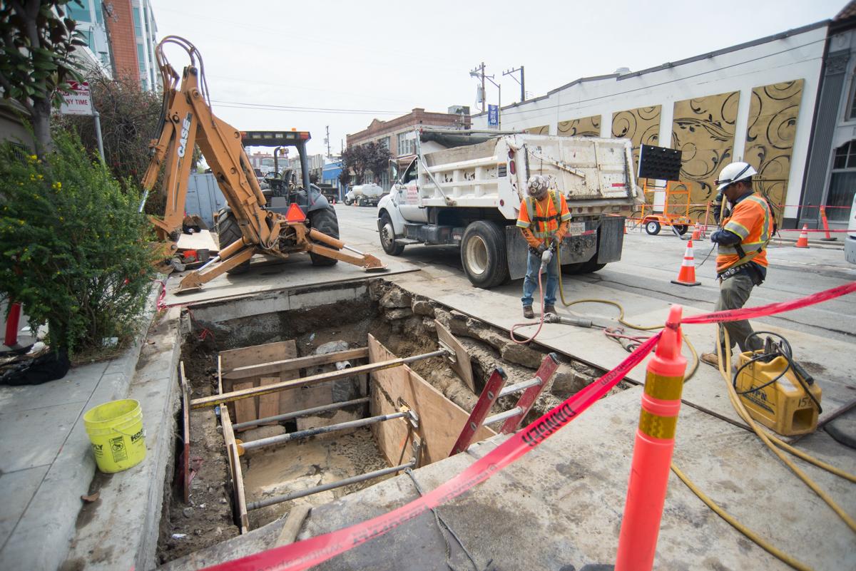 Construction workers in safety vests upgrade utilities at an excavated street section on 4th Street, with equipment and vehicles nearby.