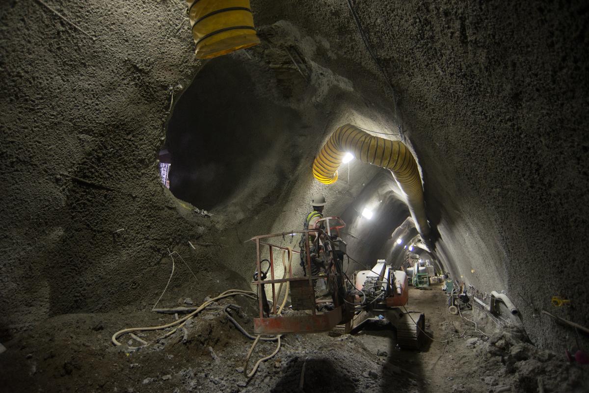Workers operate equipment inside an illuminated underground tunnel during Central Subway construction.
