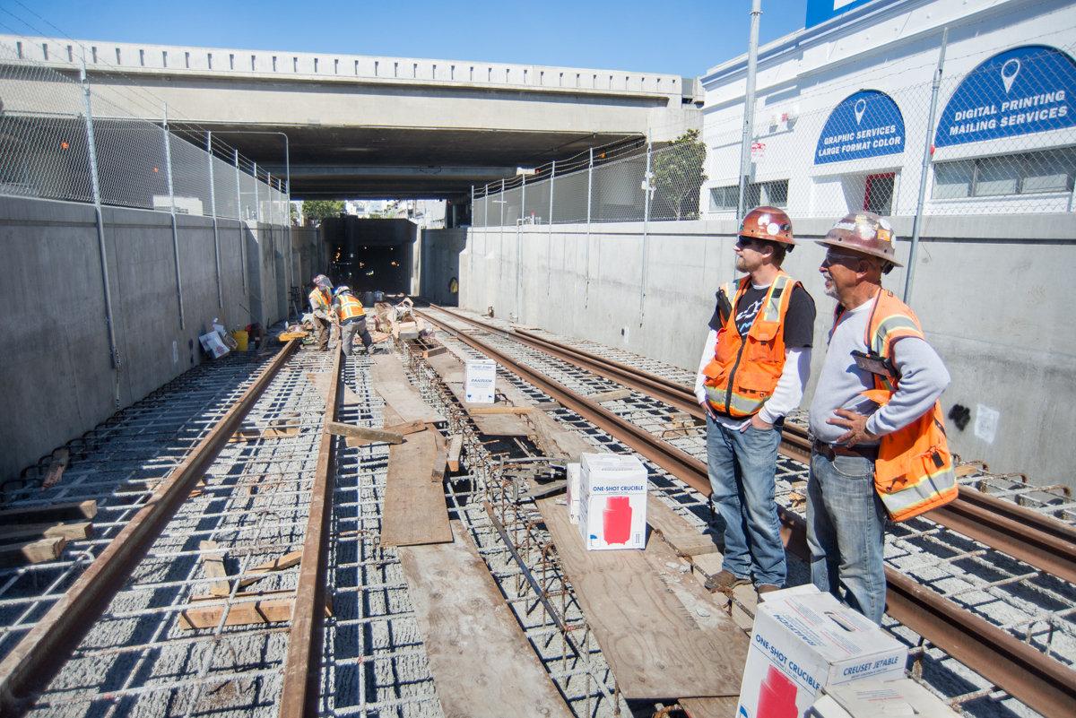 Workers in safety vests inspect railroad track installation in an underground transit tunnel.
