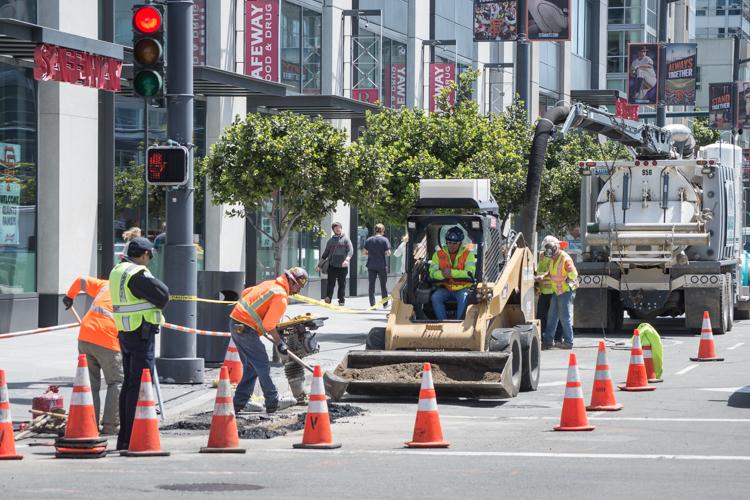 Construction workers in safety vests operate equipment on 4th Street to locate underground utilities for transit project.