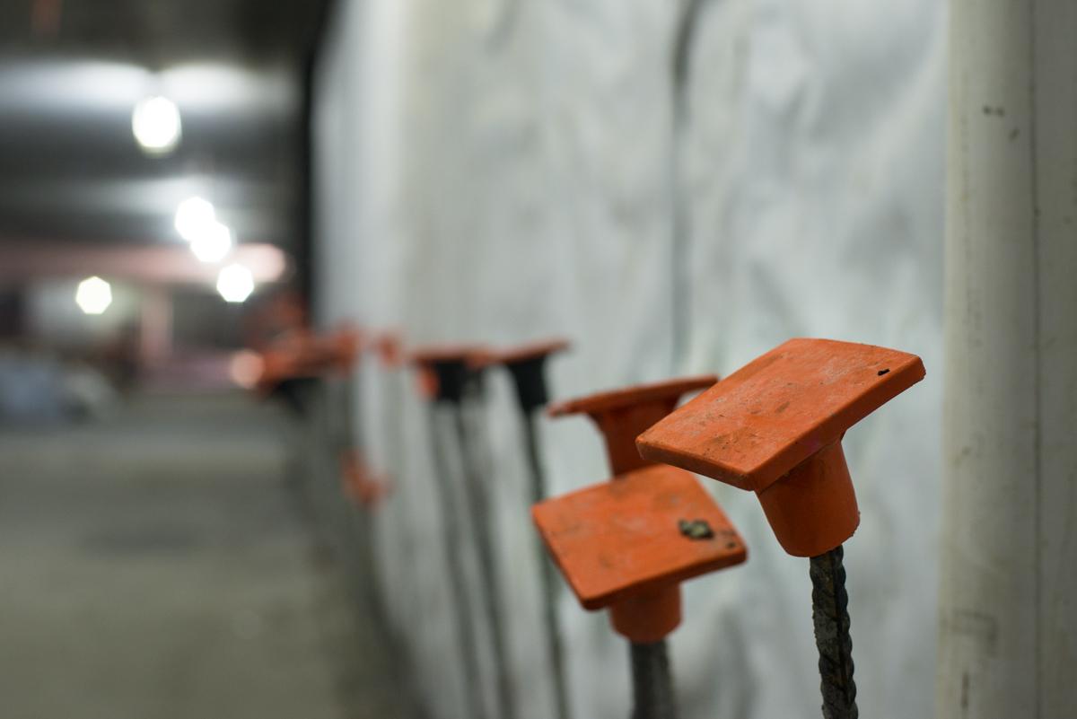 Orange metal tie-down straps attached to rebar inside station construction area.