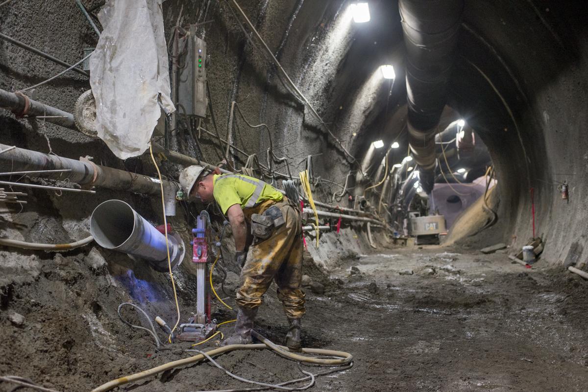 Worker in yellow safety vest welding pipe inside underground tunnel construction site with LED lighting.