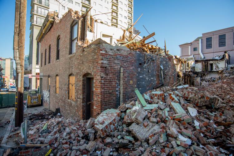Brick building under demolition with rubble and debris scattered around the site, surrounded by modern buildings.
