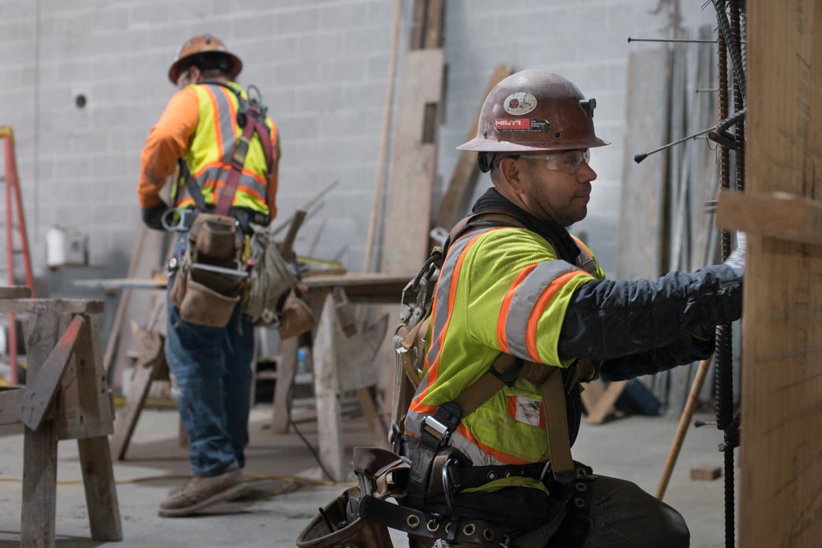 Construction workers in safety vests and hard hats install rebar and concrete forms on a building interior.