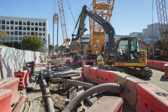 Construction site with excavator and red barriers on urban street